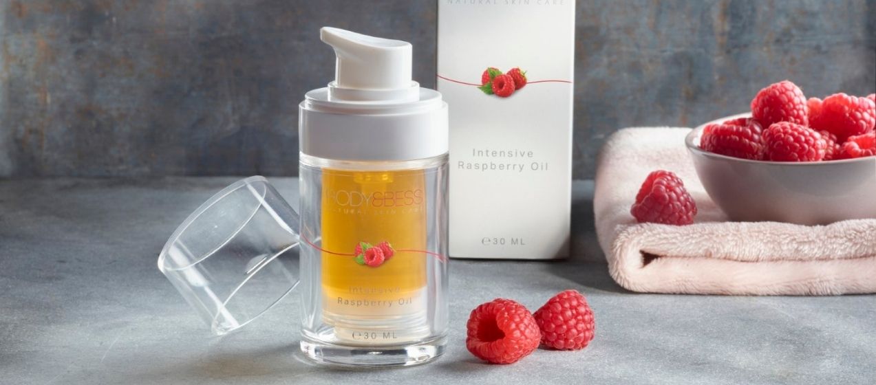Intensive Raspberry Oil met frambozen op de achtergrond.